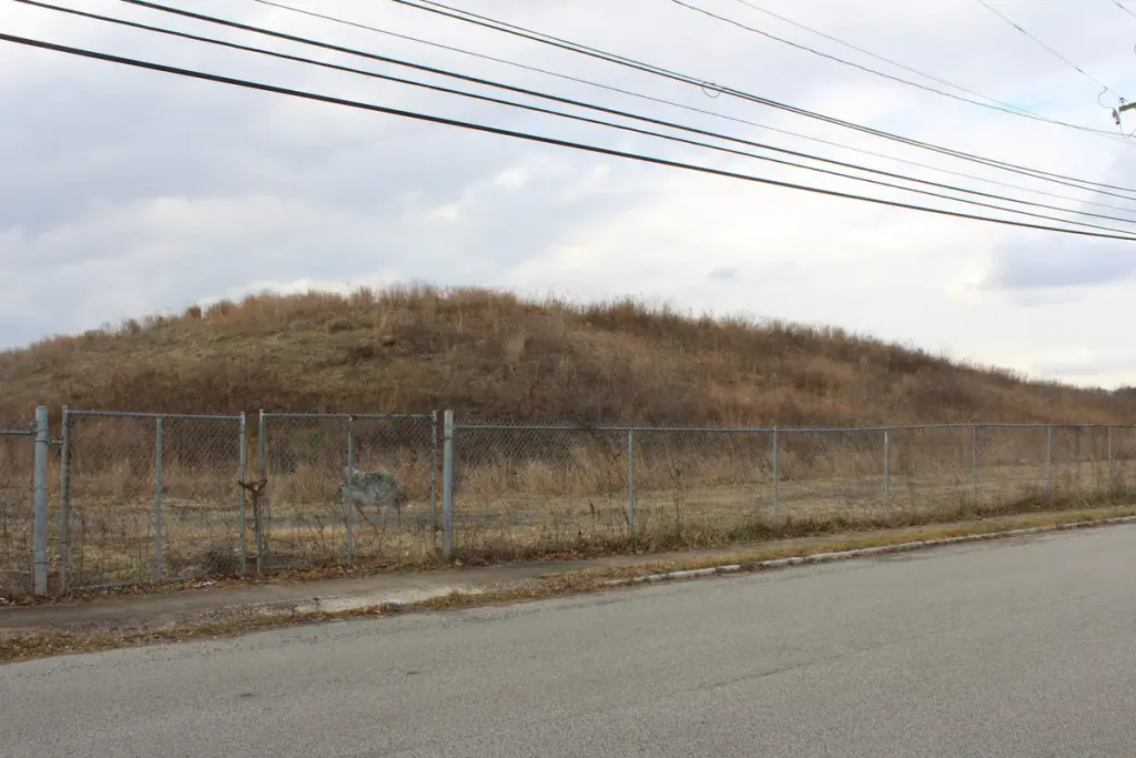 A grassed mound behind a chain-link fence, an asbestos pile capped with geotextile and clean material