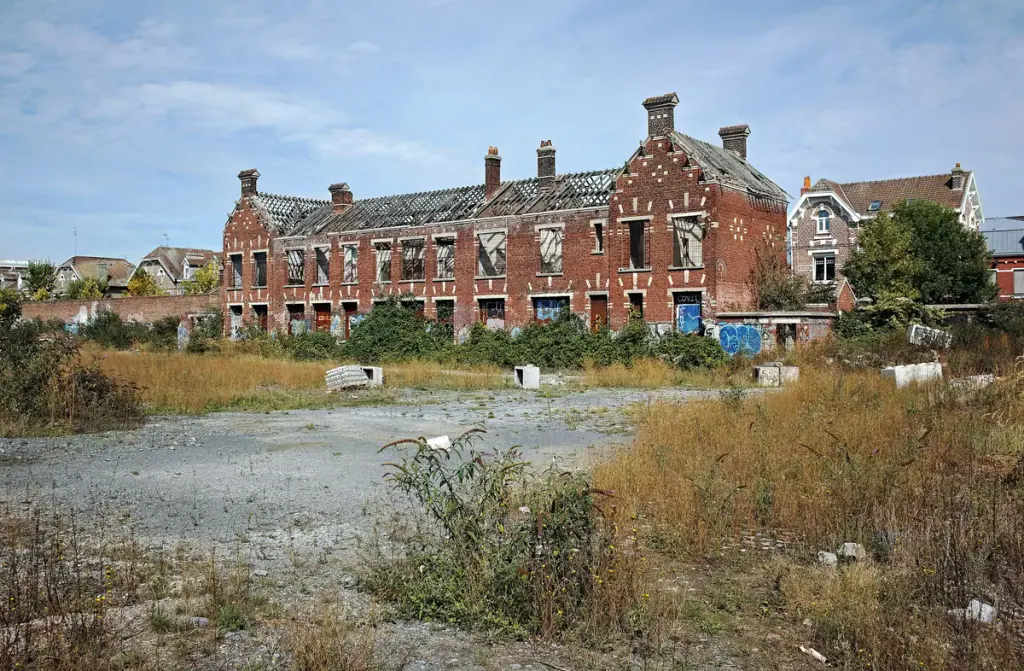 Gravel ground and weeds in front of a ruined brick building on a disused steelworks depot