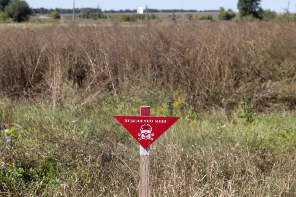 Un panneau rouge signalant des mines dans un champ ukrainien à l’abandon, envahi par les broussailles