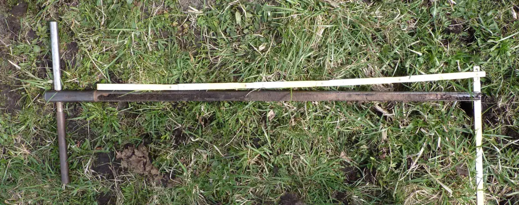 A soil probe lying on grass beside a soil core taken with it