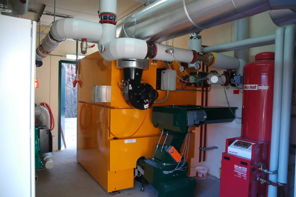 An orange wood-chip boiler with its flue pipes in a small boiler room