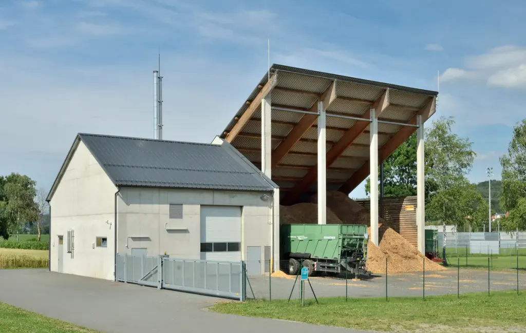 A trailer tipping wood chips under the open roof of a heating plant's chip store