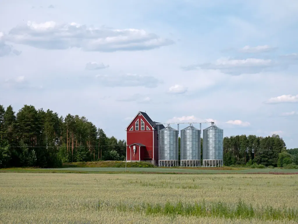 A small red dryer house and three steel grain bins at the edge of a grain field
