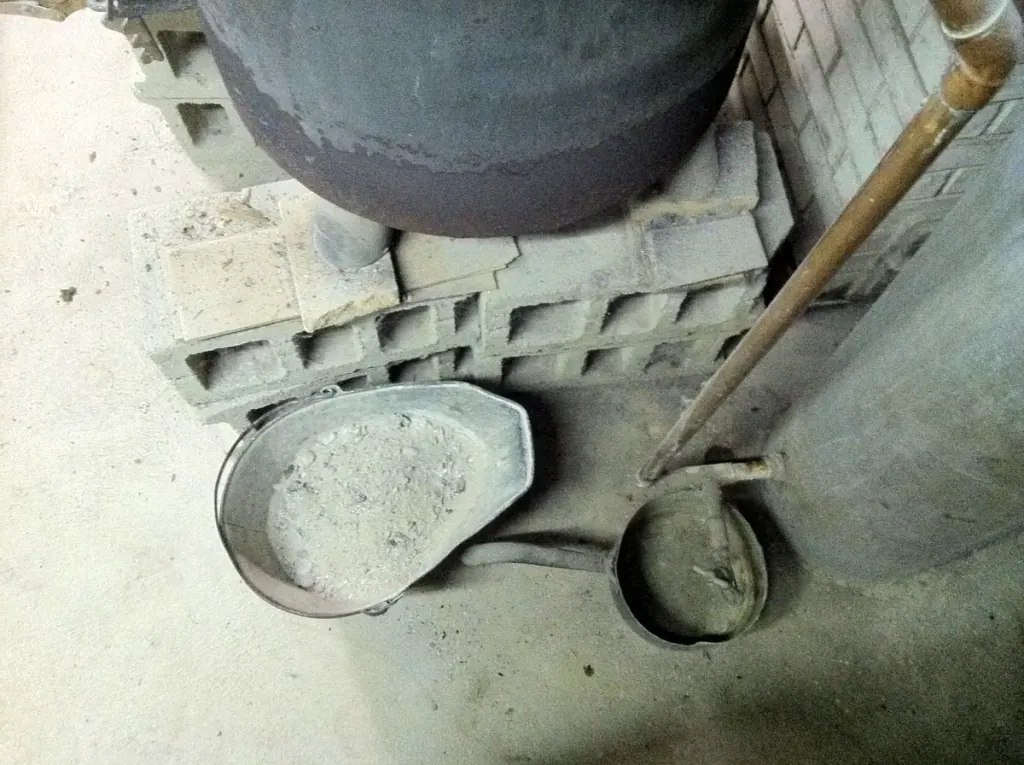 A pan of grey wood ash and a small shovel at the foot of a stove