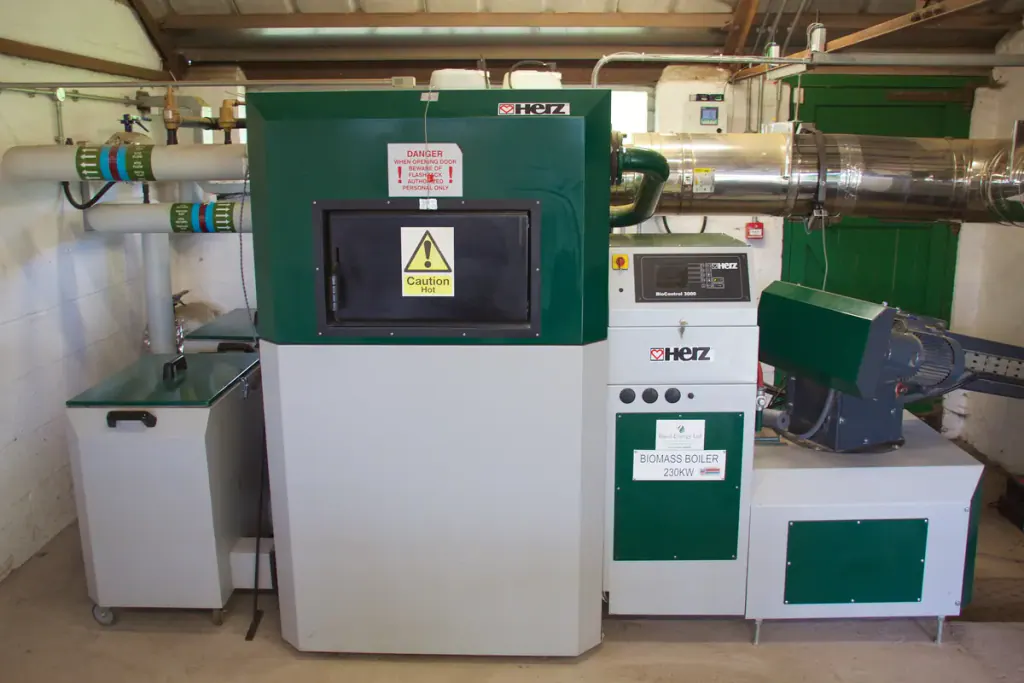 A green and white wood-chip boiler with its fuel feed in a boiler room