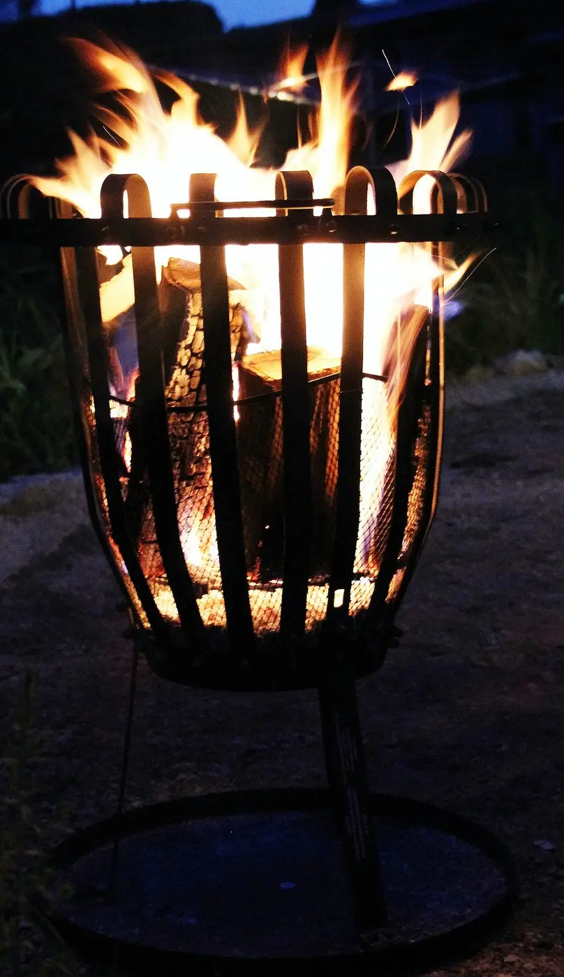 An iron fire basket with a bright flame at dusk