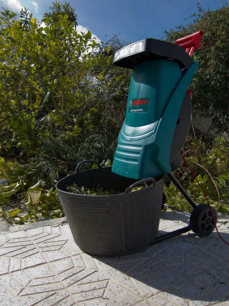 An electric garden shredder standing over a tub of chippings on a paved garden path